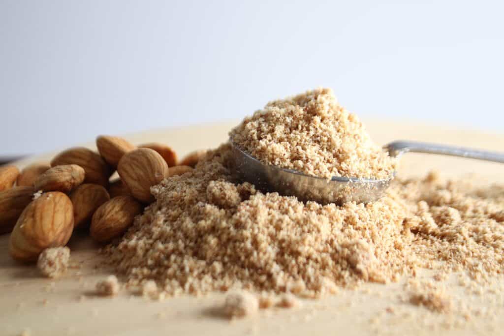 almond flour on cutting board with whole almonds and wooden spoon