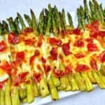 overhead closeup roasted asparagus on sheet pan with melted cheese and crispy prosciutto
