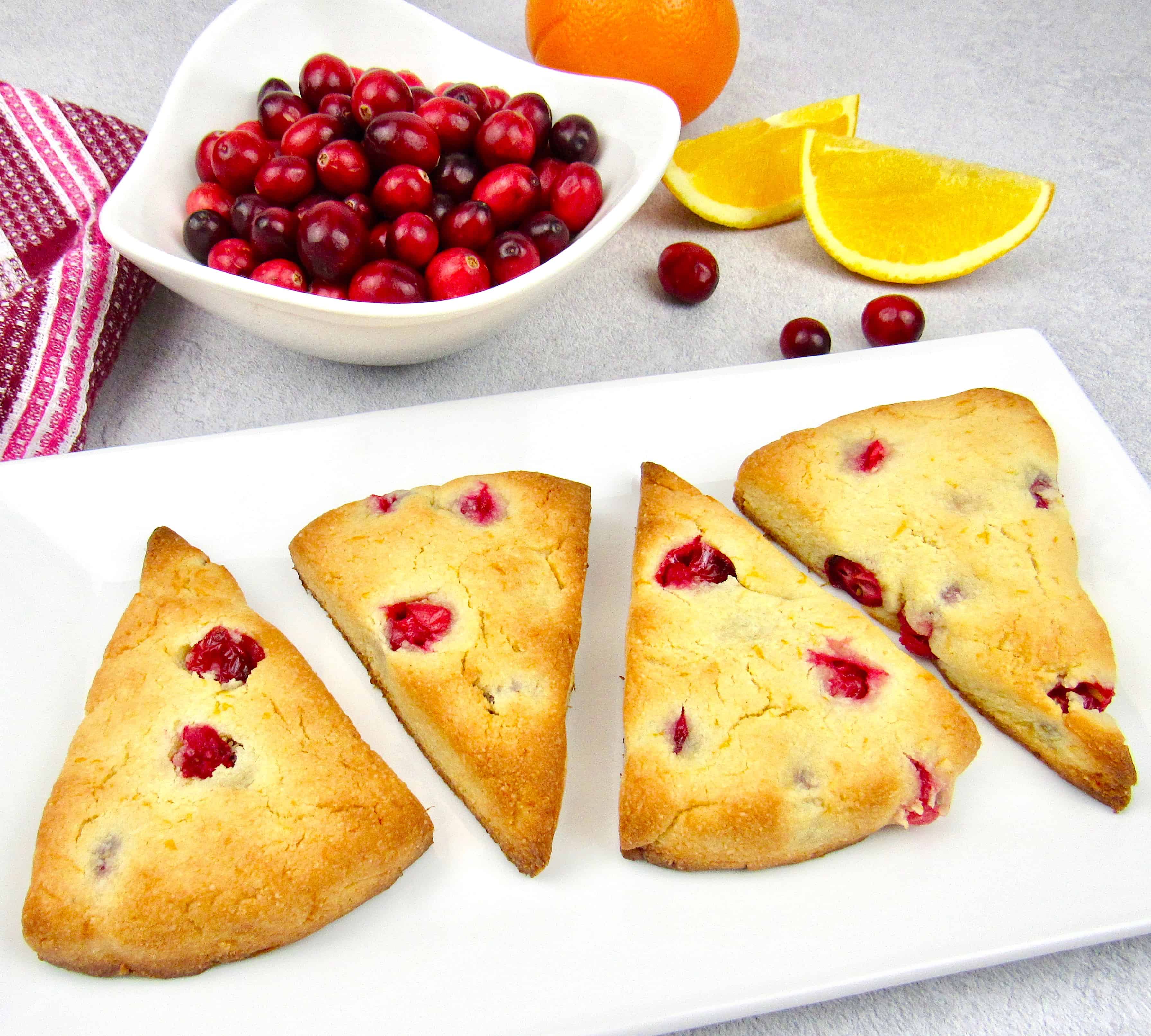 4 cranberry scones on while plate with cranberries in background