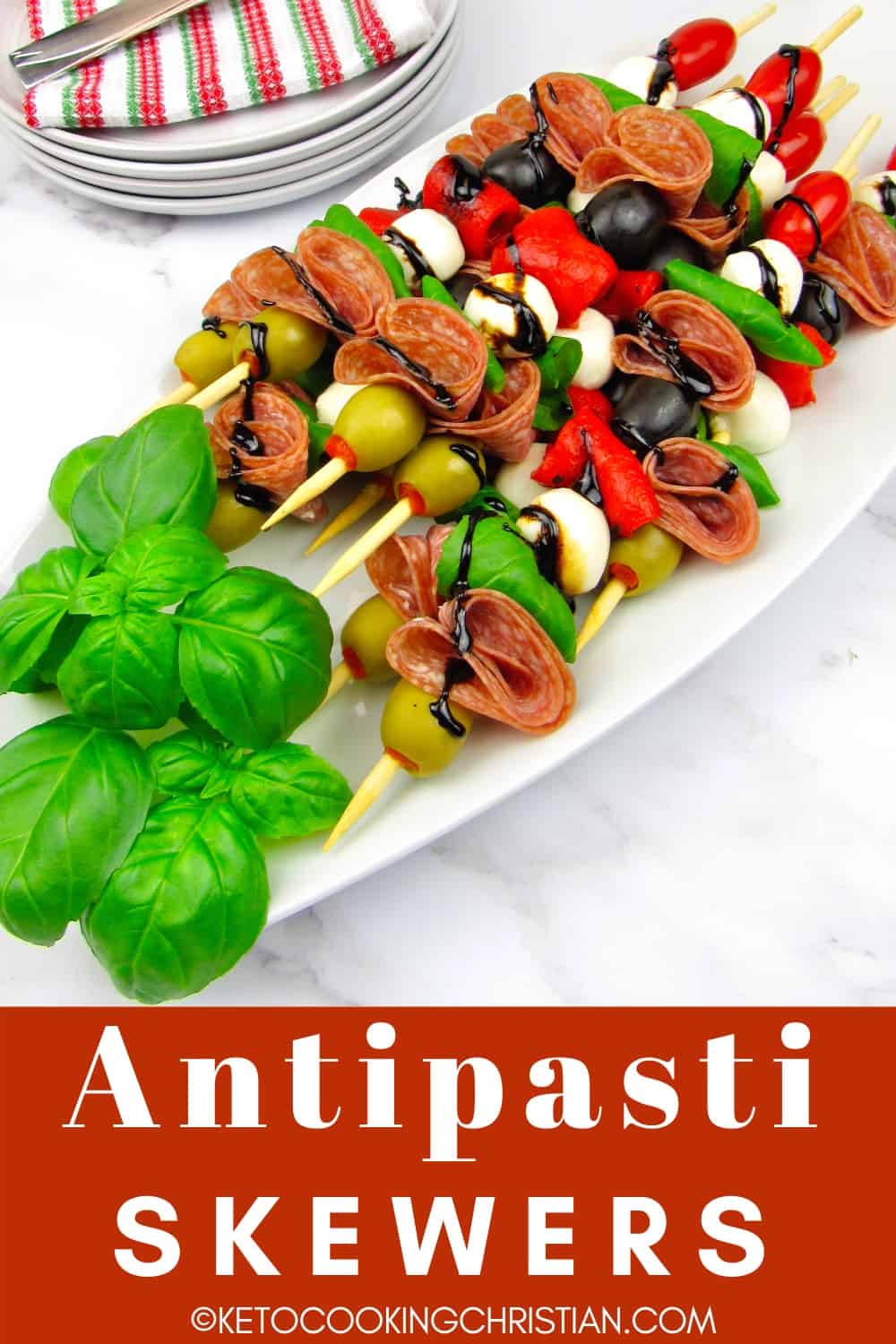 overhead view of antipasti skewers on white platter with basil leaves and balsamic glaze garnish