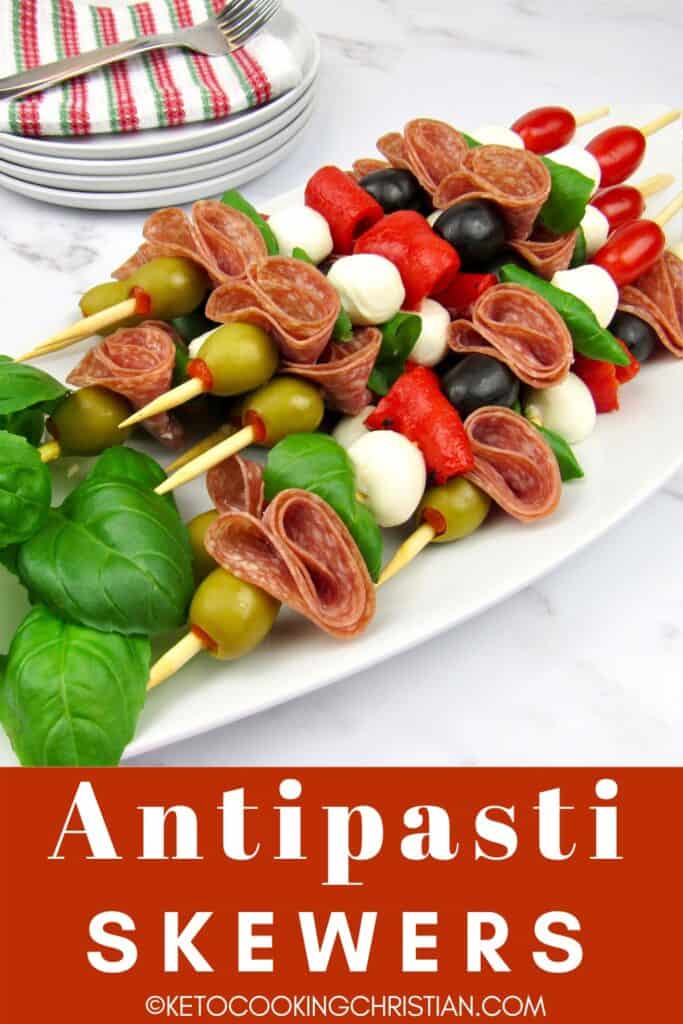overhead view of antipasti skewers on white platter with basil leaves garnish