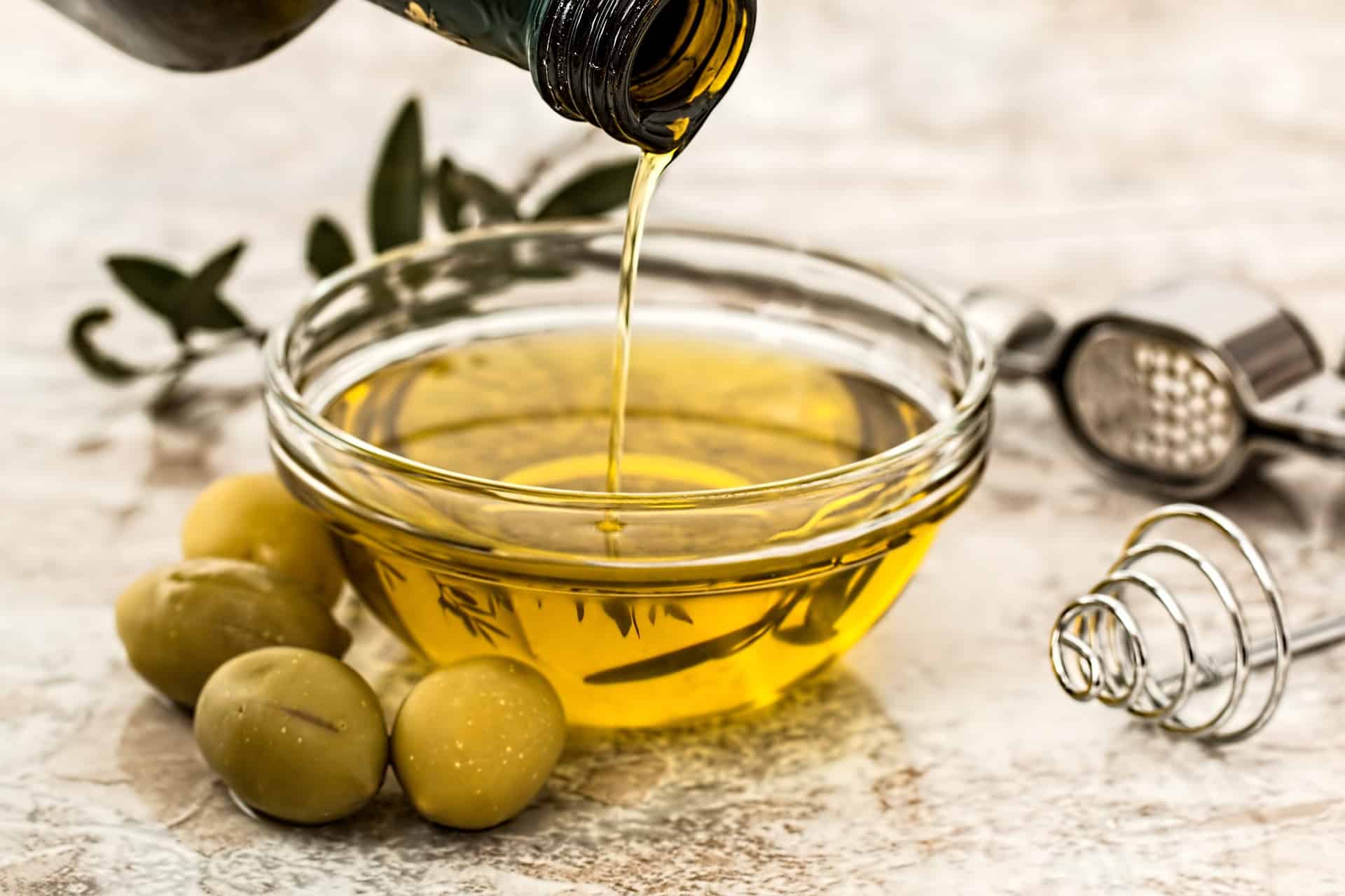 olive oil poured into glass bowl with green olives on the side