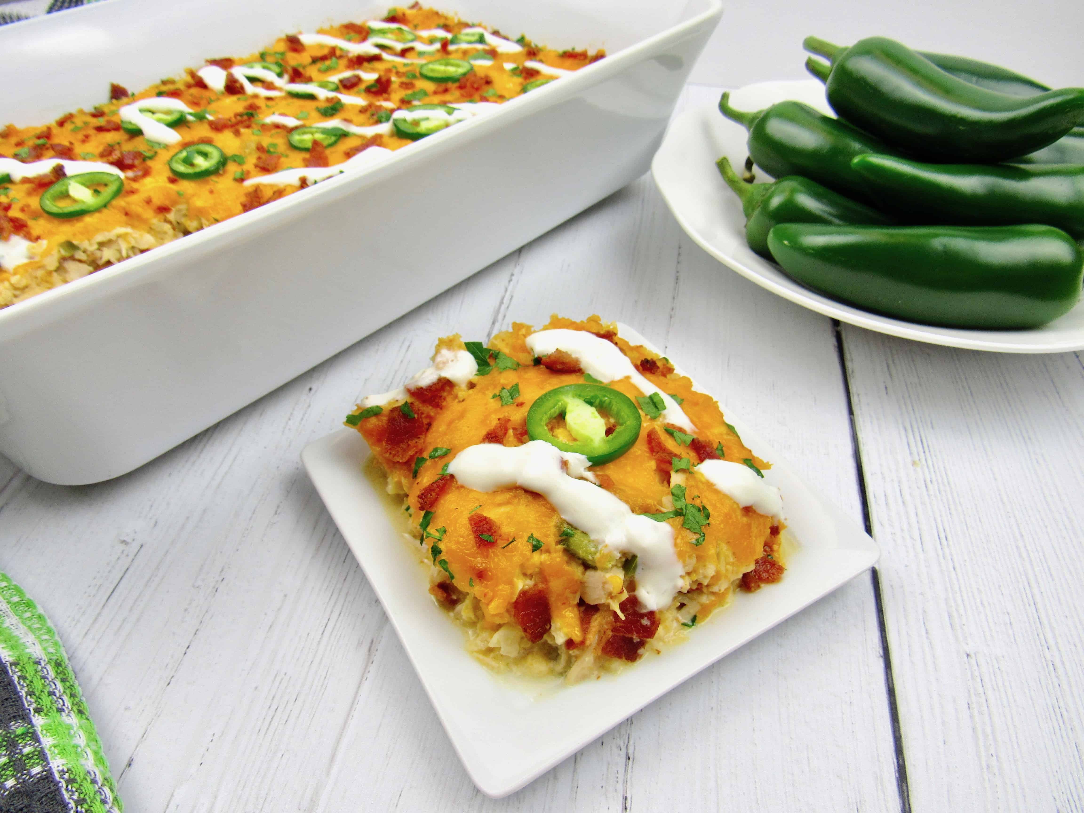 slice of jalapeno popper chicken casserole with casserole and bowl of peppers in background