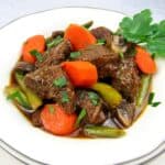 closeup of instant pot beef stew in white bowl with parsley garnish