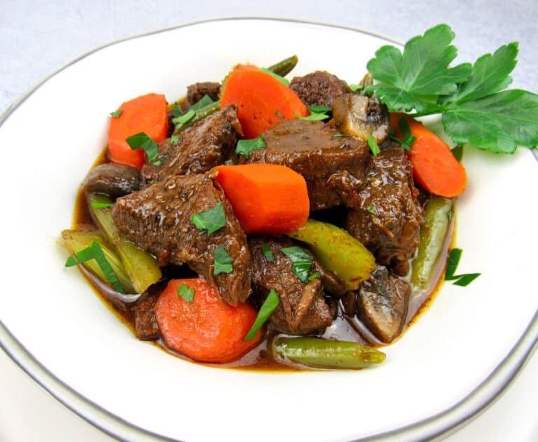 closeup of instant pot beef stew in white bowl with parsley garnish