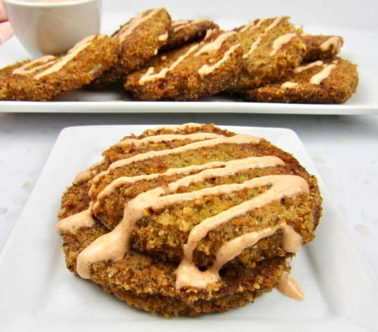closeup of 2 fried green tomatoes on white plate with sauce drizzled on top
