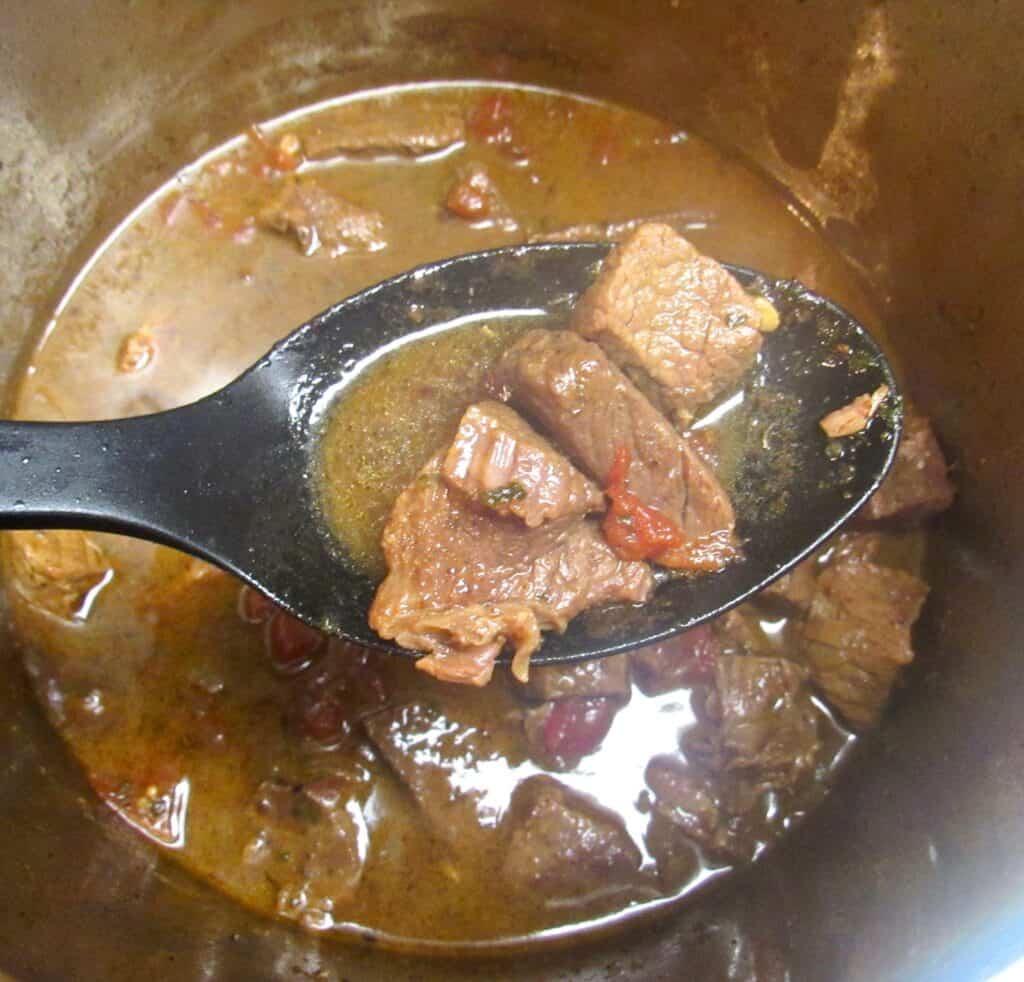 beef stew meat held up with black serving spoon