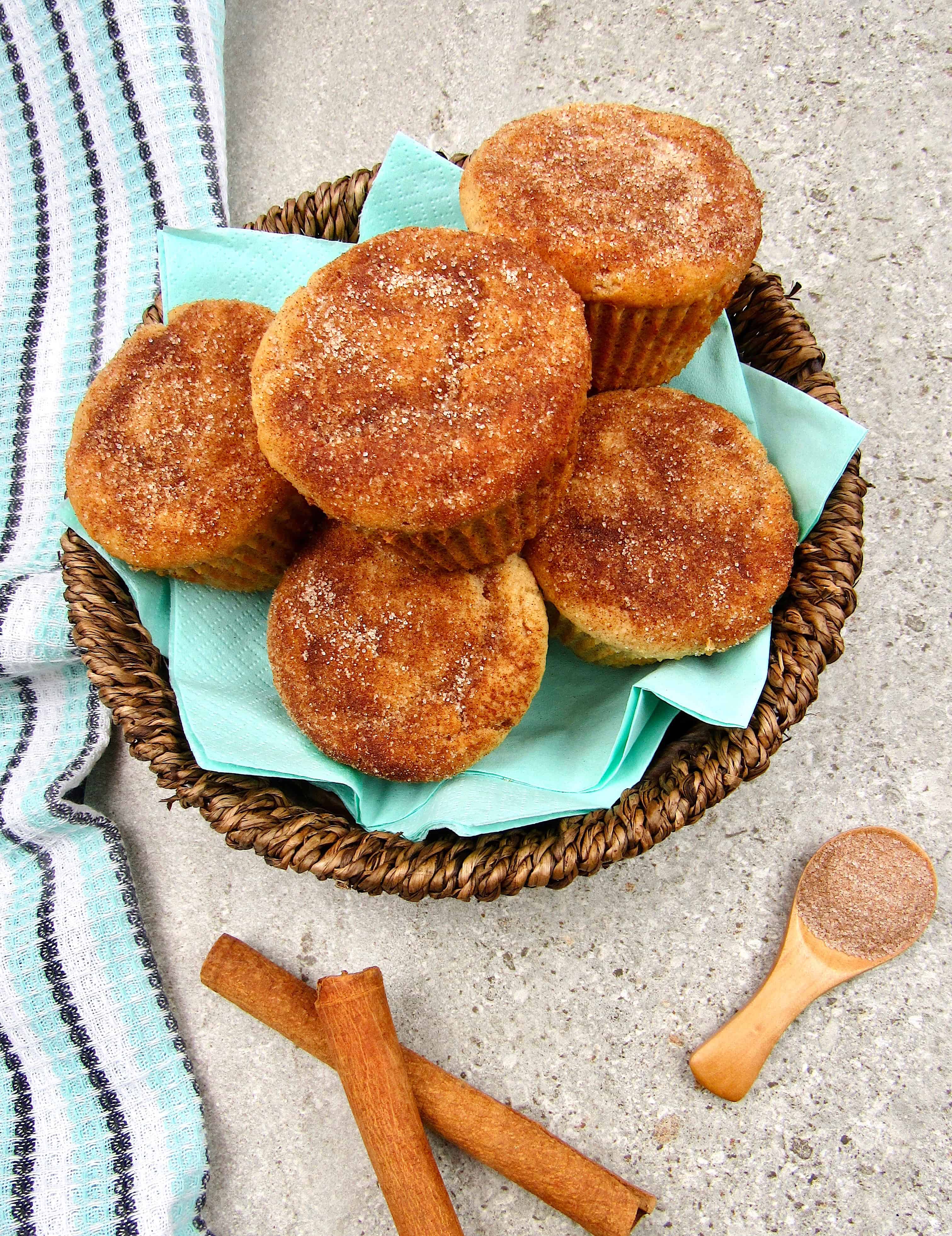overhead view of snickerdoodle muffins in basket with cinnamon sticks on side