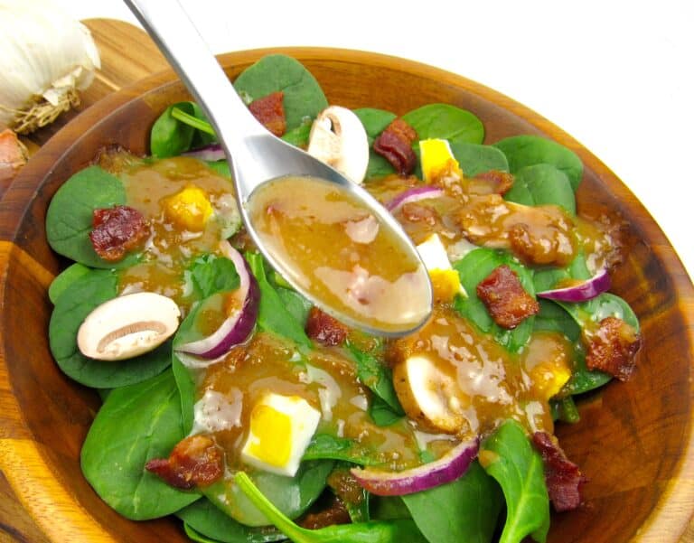 spoonful of hot bacon dressing over spinach salad