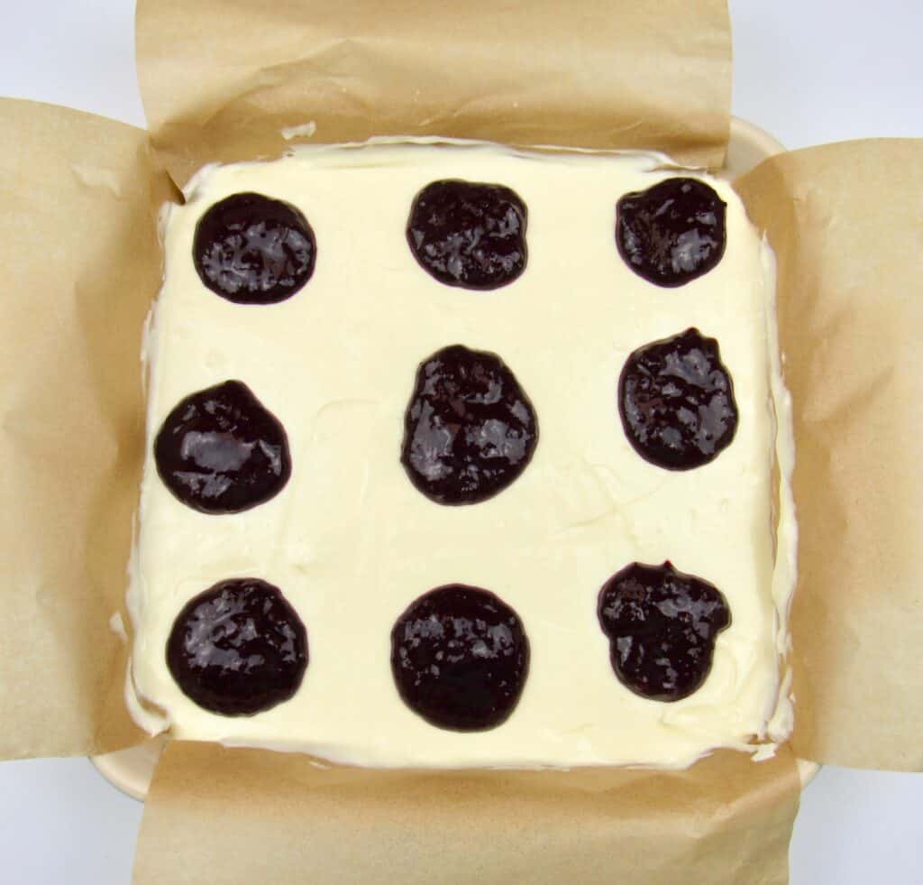 cheesecake bars batter with dollops of blueberry sauce