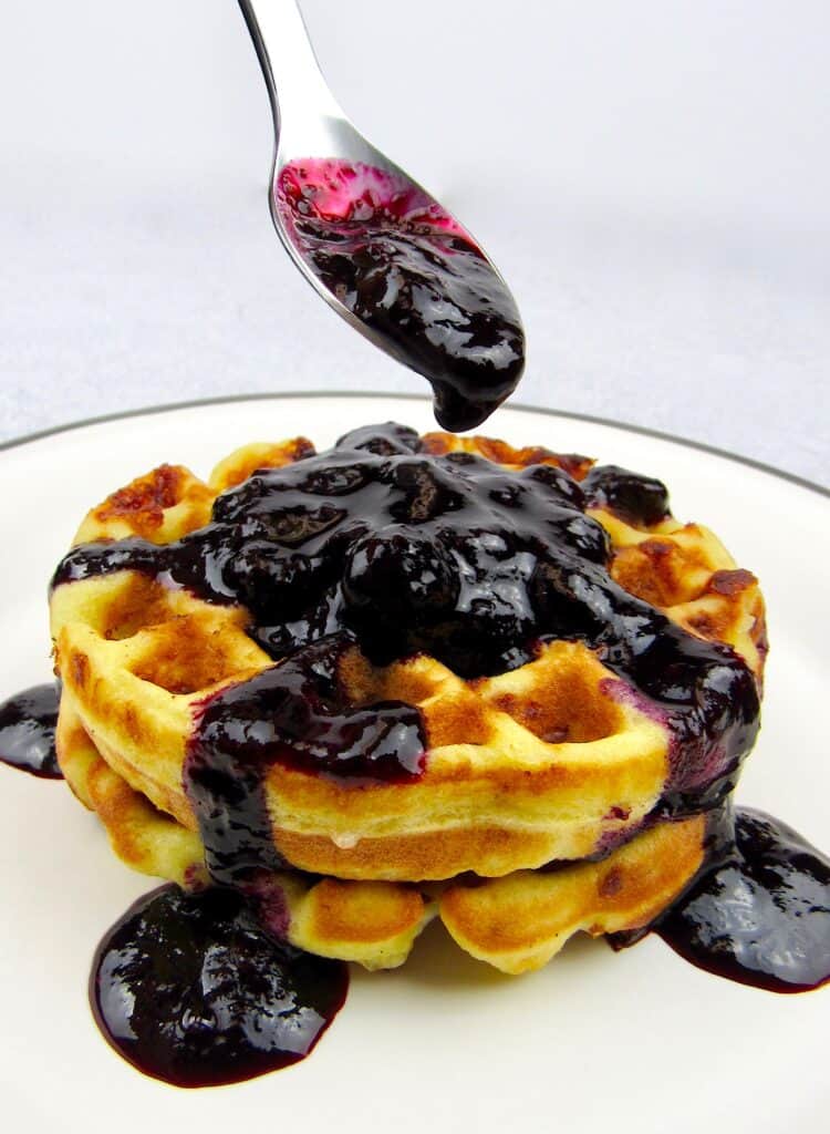 closeup of blueberry sauce in spoon over waffles