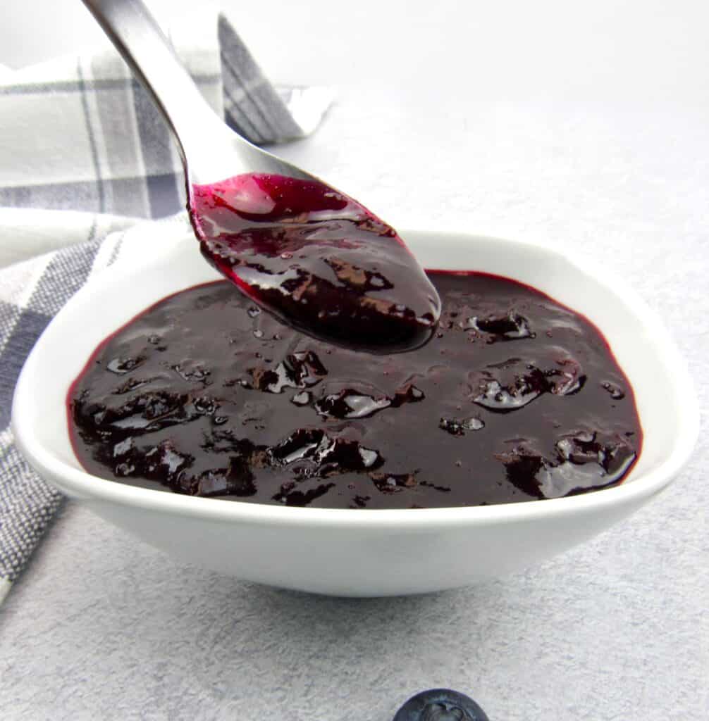 blueberry sauce in white dish with spoon holding some up