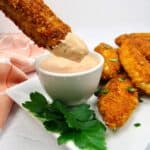 chicken tenders on white plate ong being dipped into dipping sauce