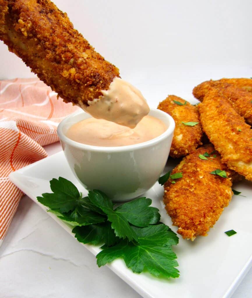 chicken tenders on white plate ong being dipped into dipping sauce