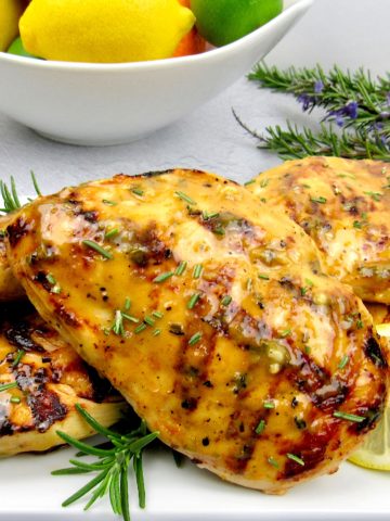 closeup of citrus glazed grilled chicken with bowl of fruit in background