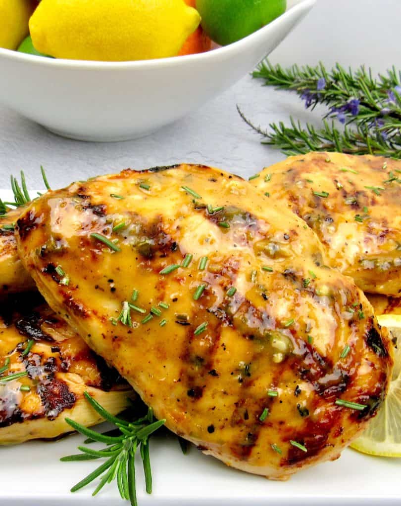 closeup of citrus glazed grilled chicken with bowl of fruit in background