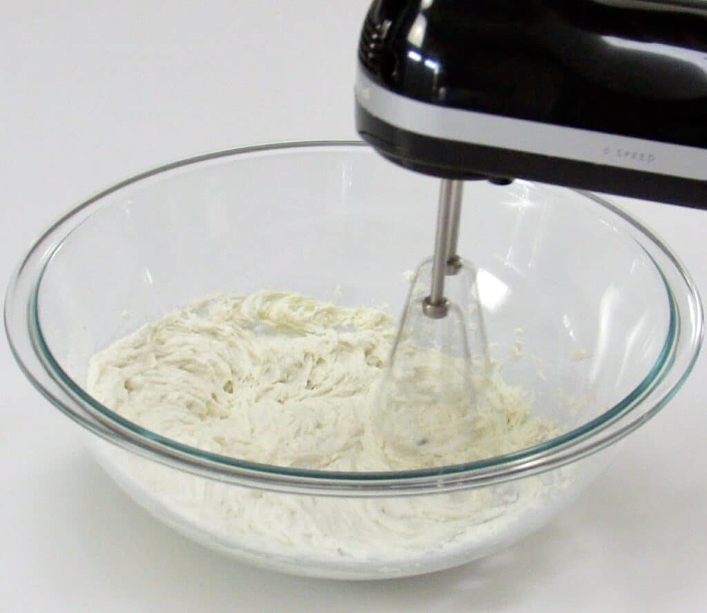 whipped coconut cream in glass bowl being mixed with hand mixer