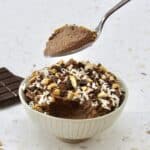 bowl of chocolate mousse with coconut and almonds on top and spoon holding up some
