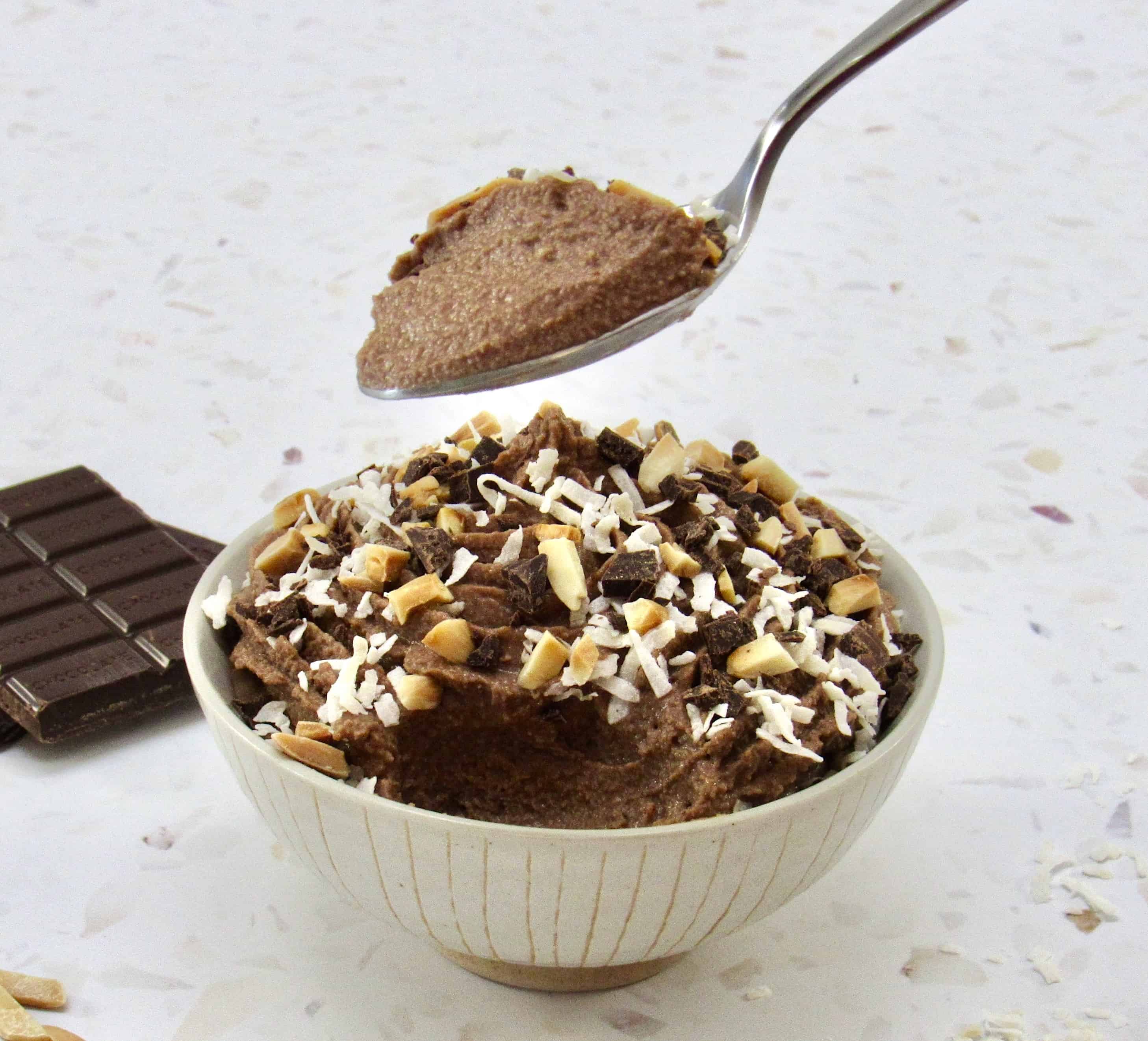 bowl of chocolate mousse with coconut and almonds on top and spoon holding up some
