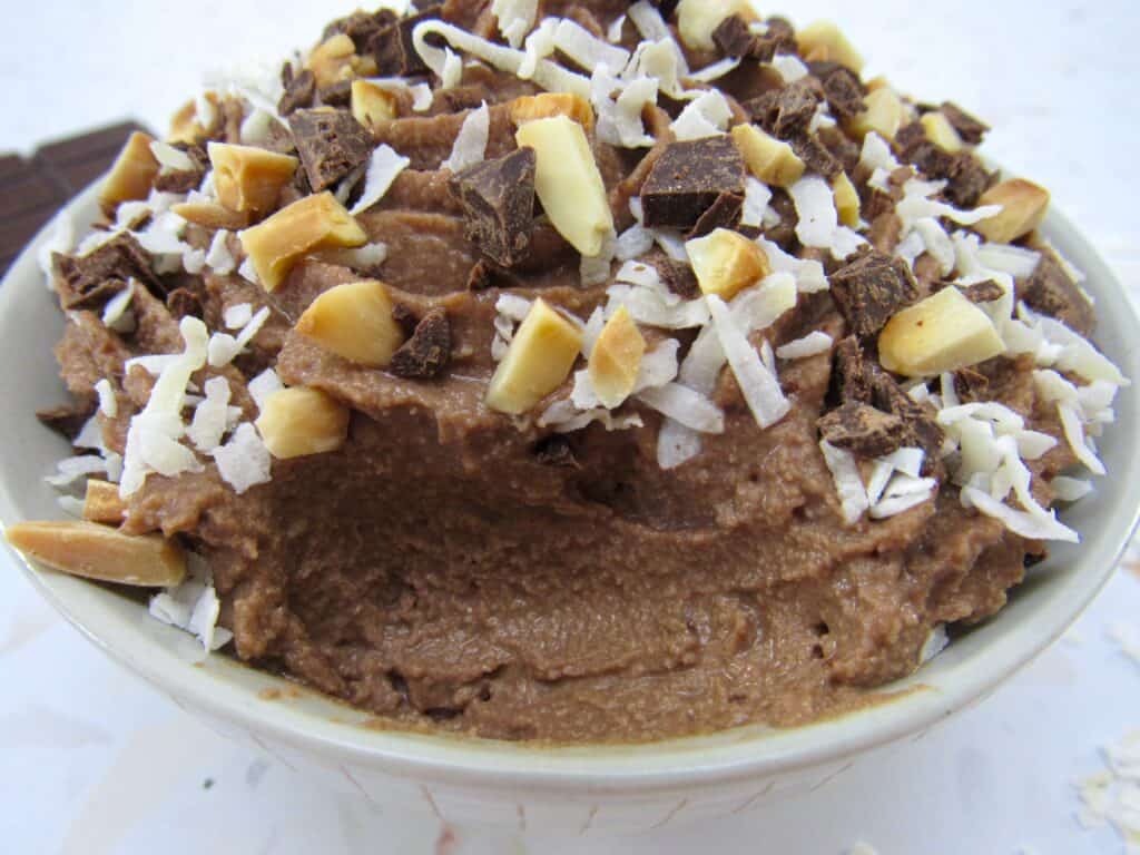 bowl of chocolate mousse with coconut and almonds on top with a spoonful missing