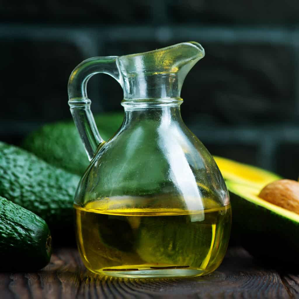 Avocado Oil in glass dressing bottle with avocados in background