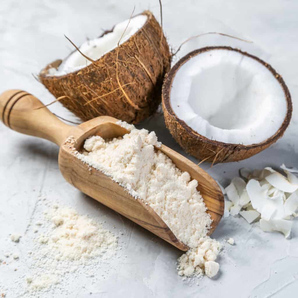 Coconut Flour in a wooden scoop with fresh coconut in background