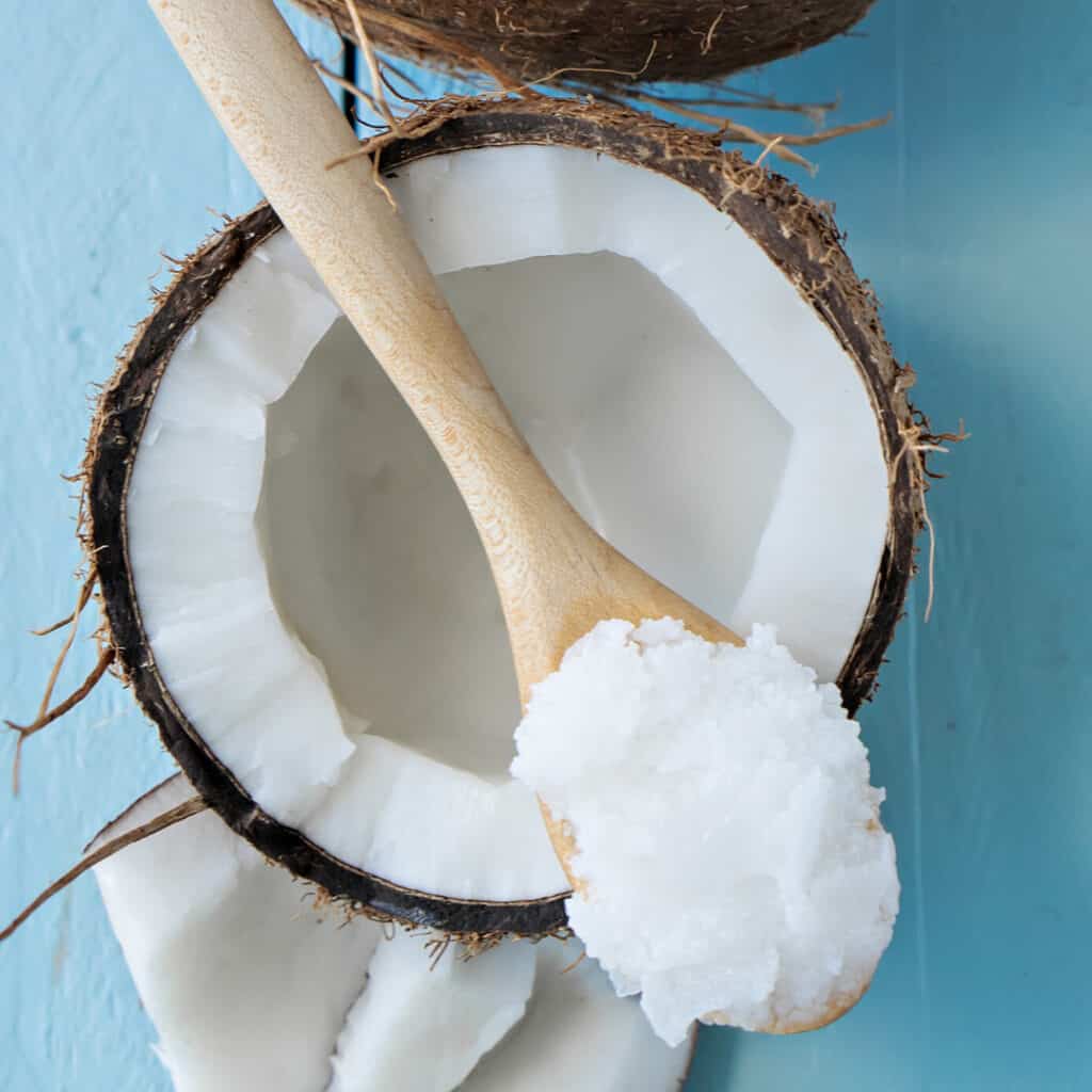 Coconut Oil in wooden spoon sitting on open coconut