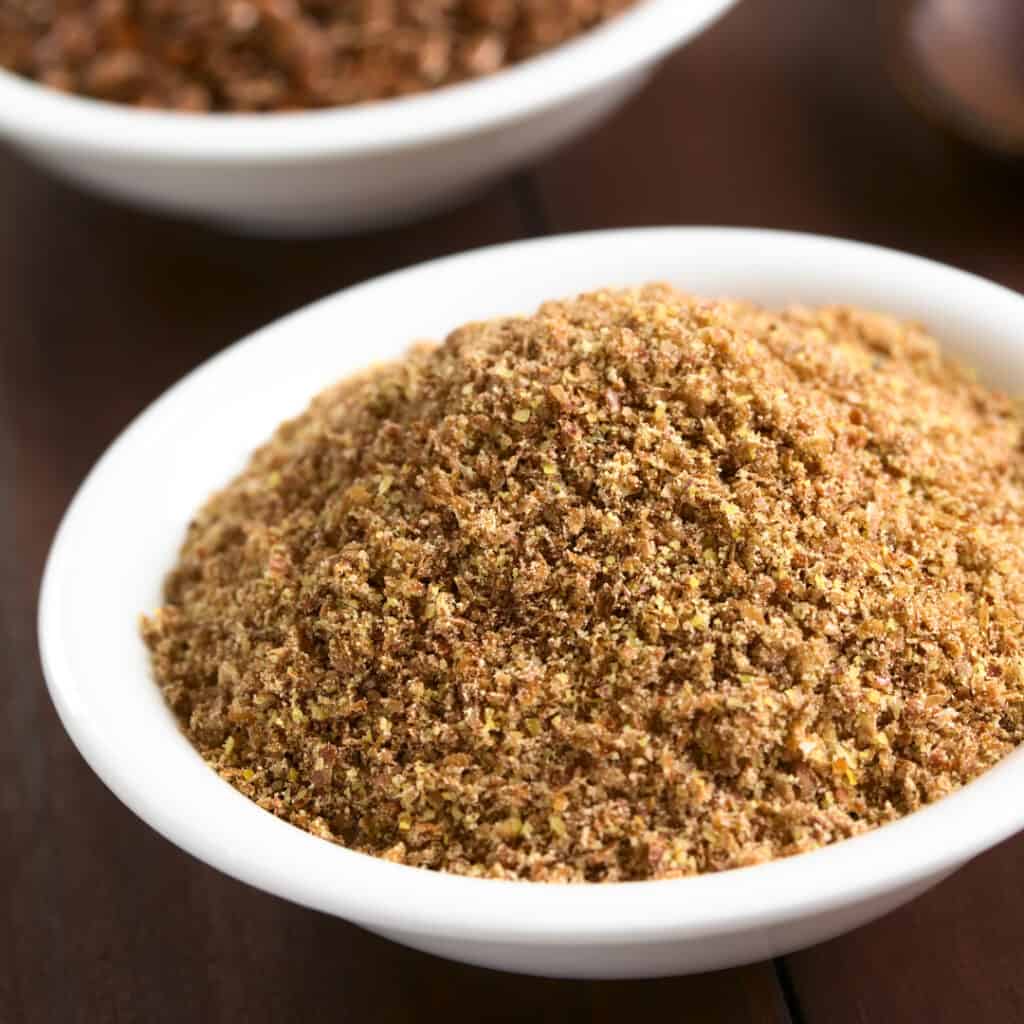 Flax Meal in white bowl with flax seeds in background