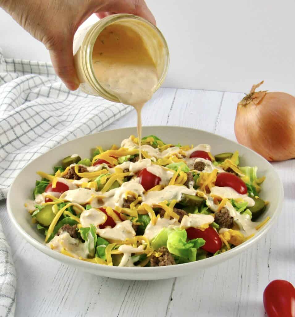 cheeseburger salad with dressing being poured over the top