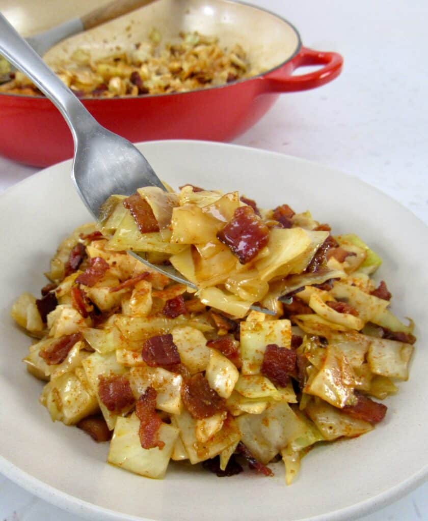 closeup of fried cabbage with bacon in beige bowl with fork holding up some