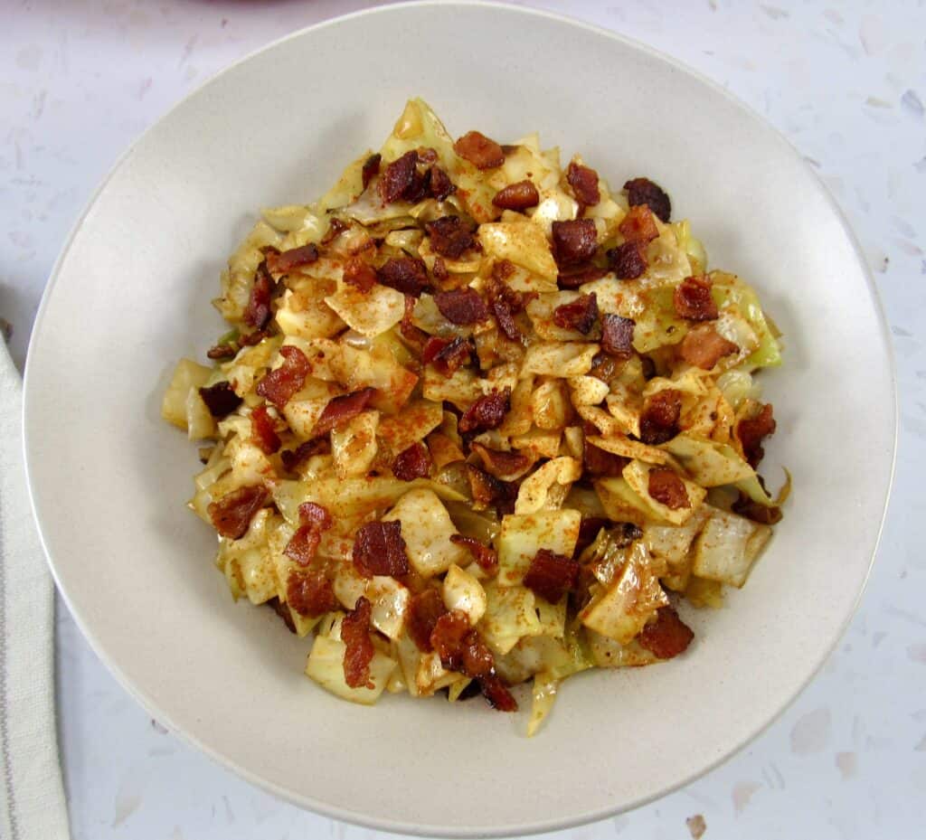 overhead view of fried cabbage with bacon in beige bowl