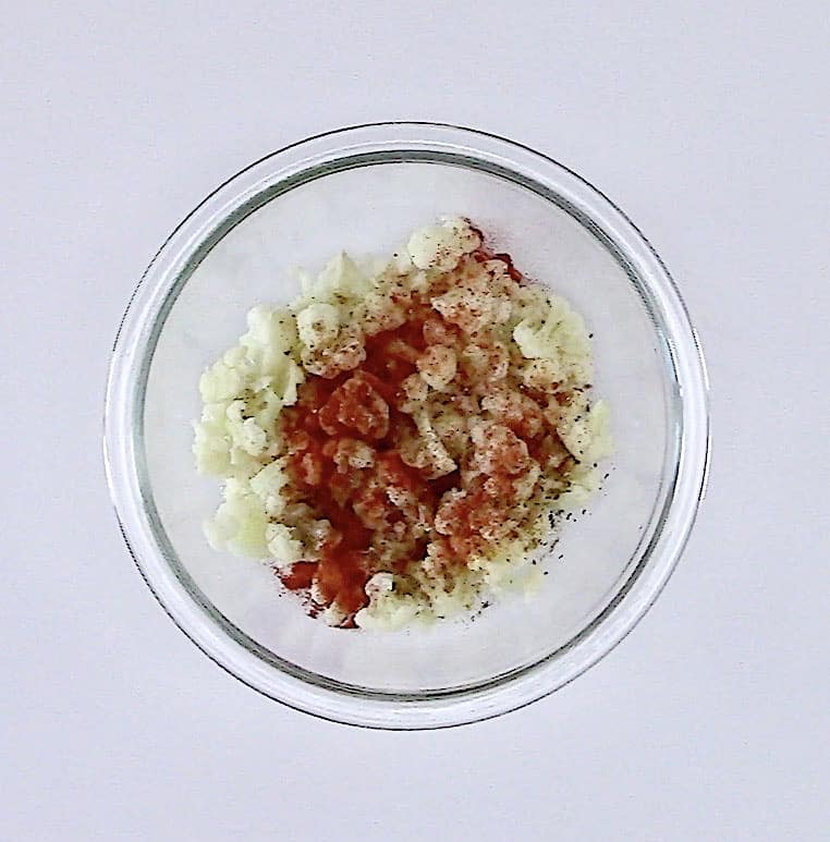cauliflower florets with spices on top in glass bowl