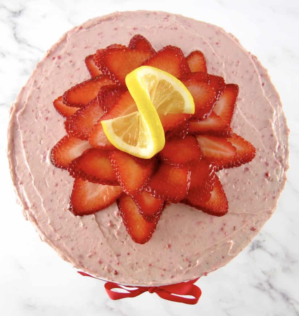 overhead view of strawberry cake with strawberries on top and slice of lemon