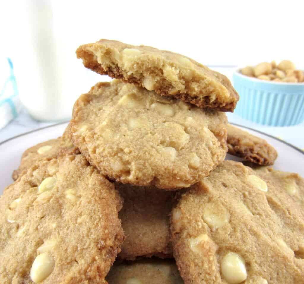 pile of white chocolate macadamia nut cookies on plate with a broken cookie on top