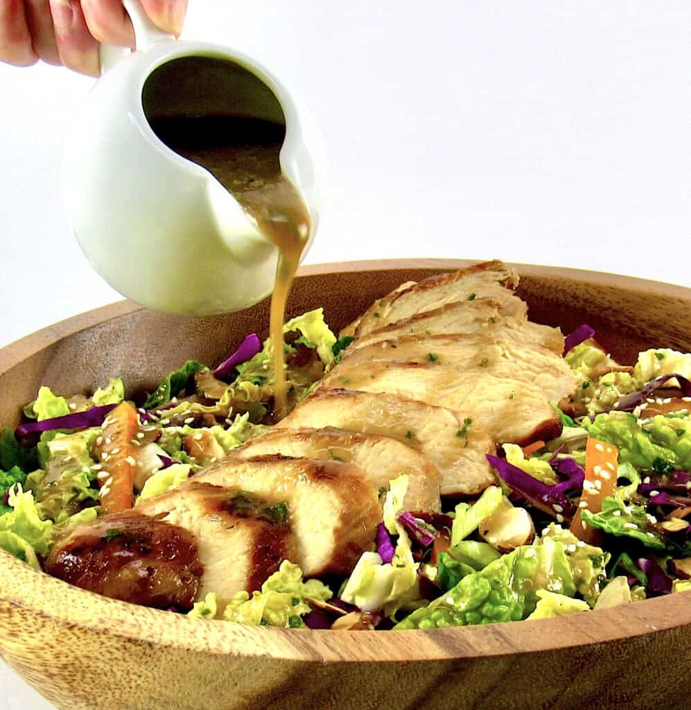 dressing being poured over sliced chicken salad