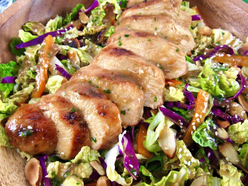 closeup of sliced grilled chicken over a salad