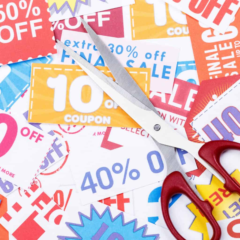 pile of coupons with a pair of red scissors on top