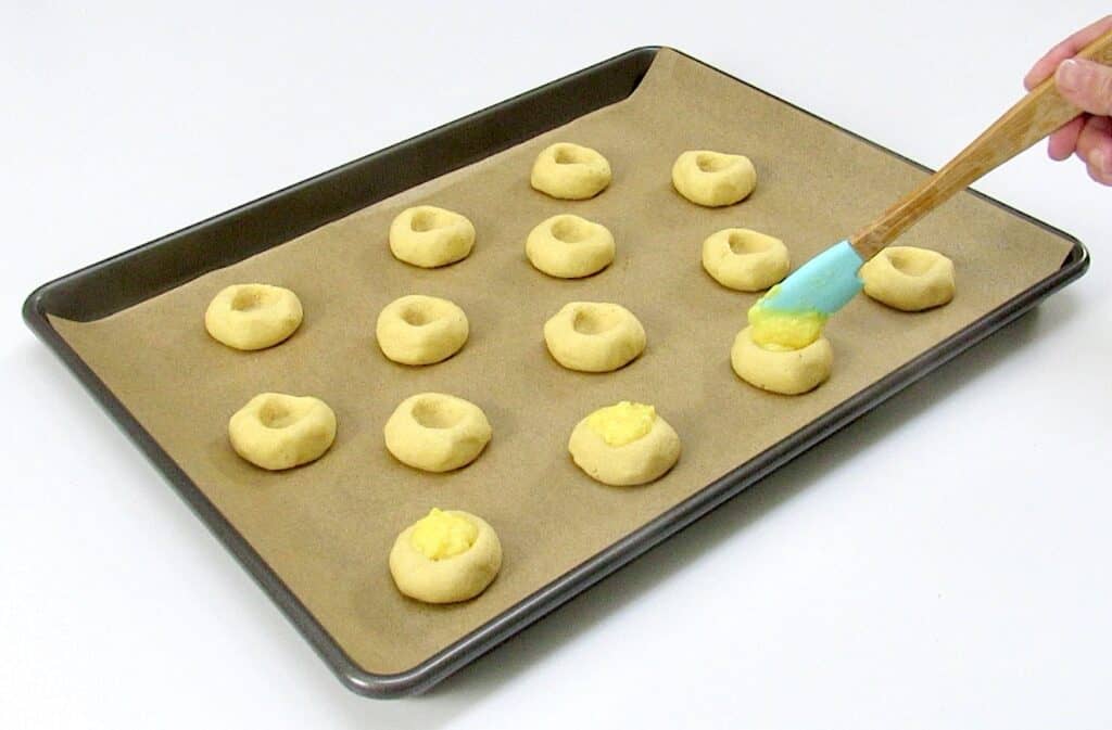 thumbprint cookies on baking sheet being filled with lemon curd