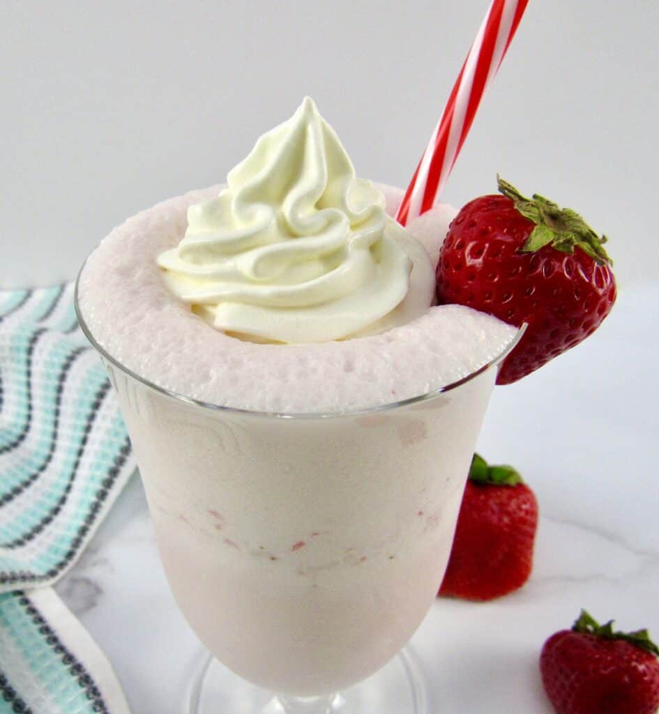 closeup of strawberry smoothie with whip cream and strawberry on glass
