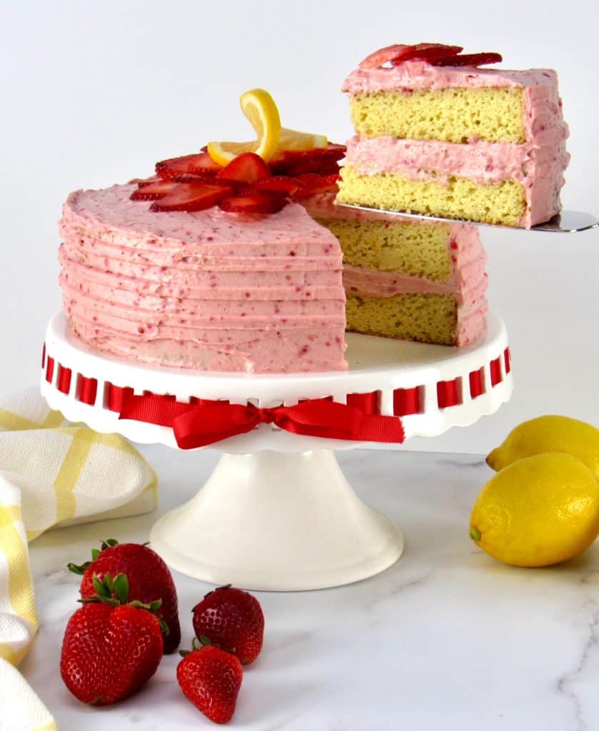 strawberry cake on cake stand with strawberries on top with slice held up