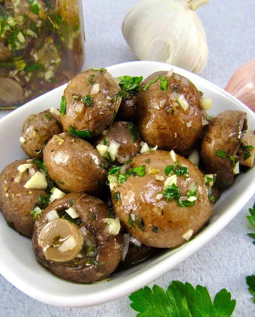 white bowl with marinated mushrooms, garlic and jar in background
