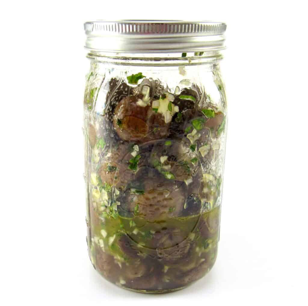 mushrooms in glass jar mixed with marinade