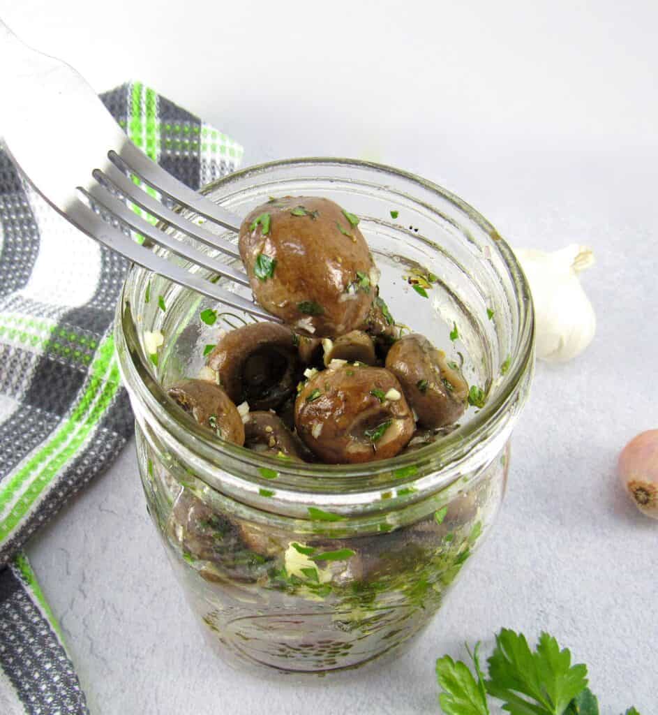 Marinated Mushrooms in glass jar with fork holding one up