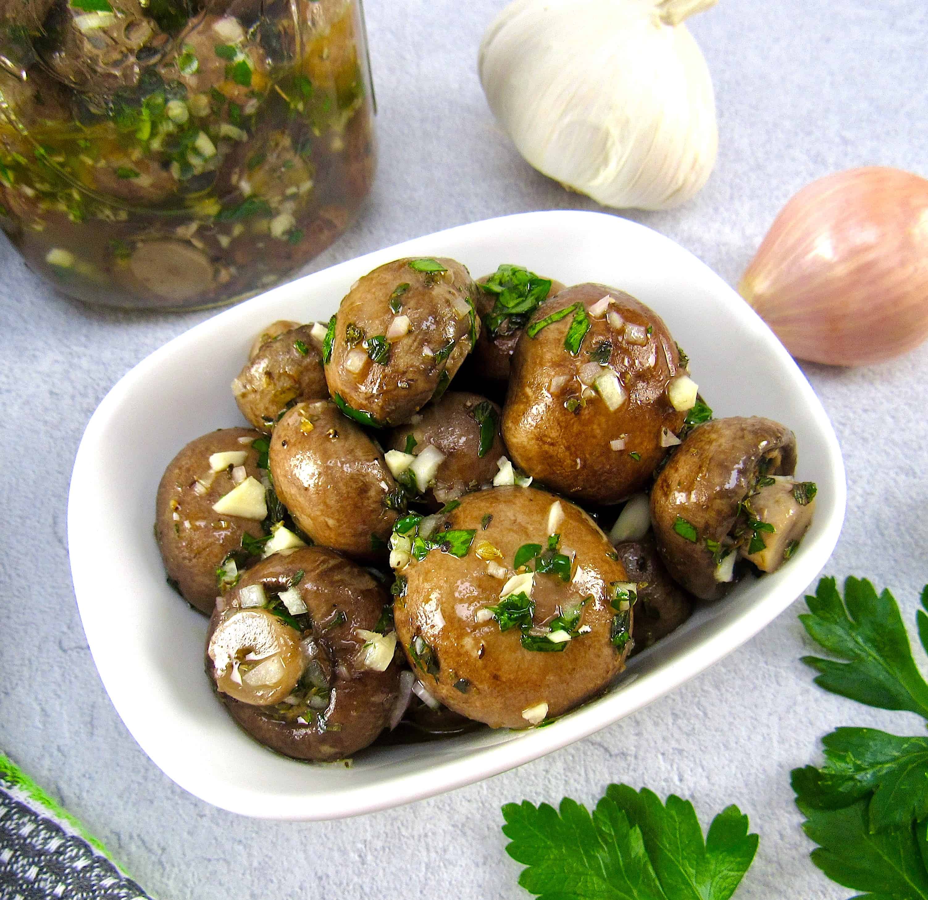 white bowl with marinated mushrooms, garlic and jar in background