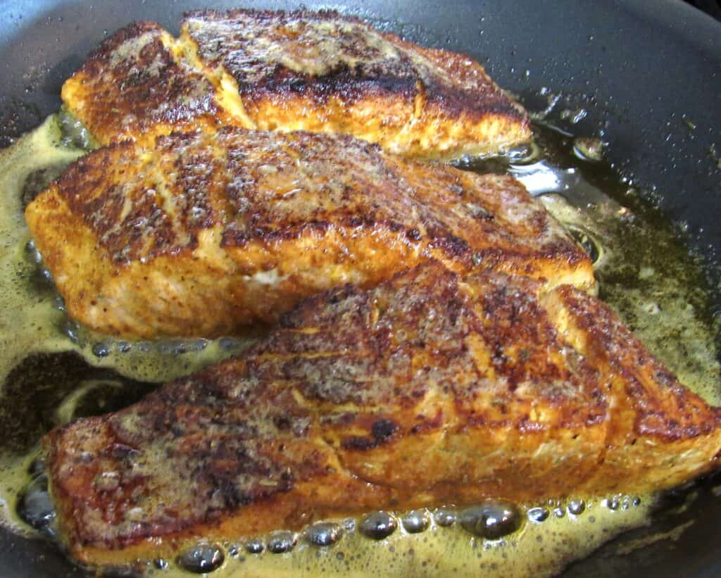 3 pieces of blackened salmon cooking in skillet