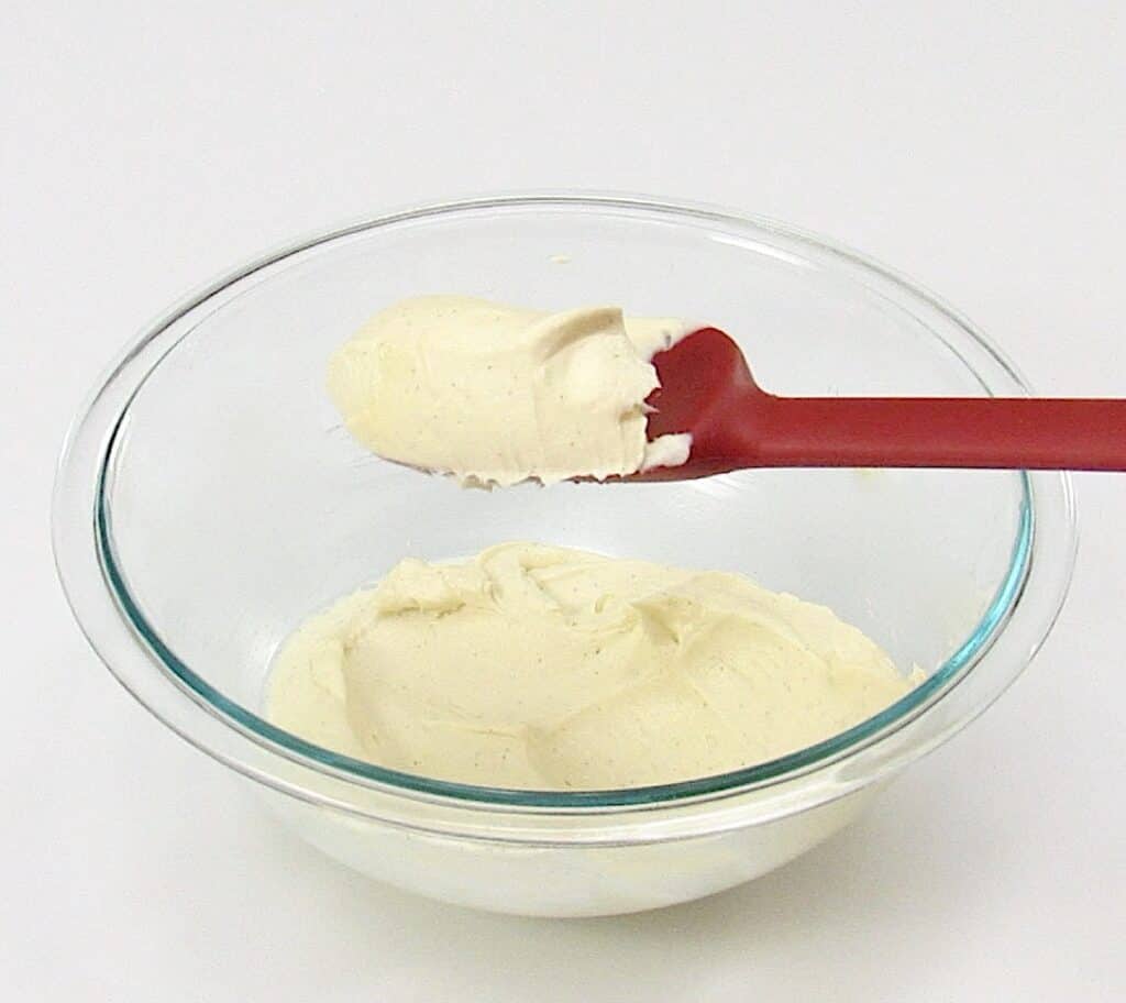 vanilla frosting in glass bowl with red spoon holding up some