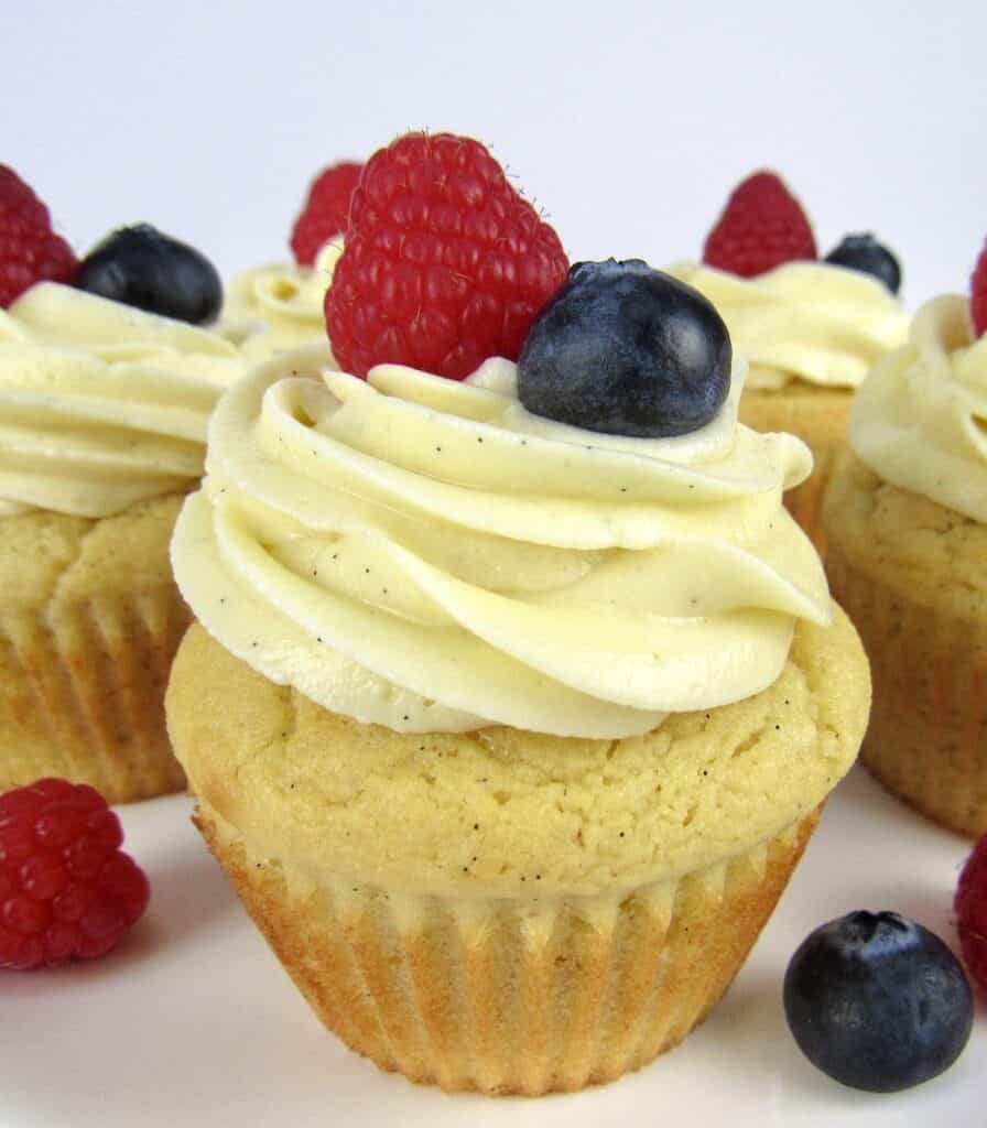 closeup of vanilla cupcake with raspberry and blueberry on top