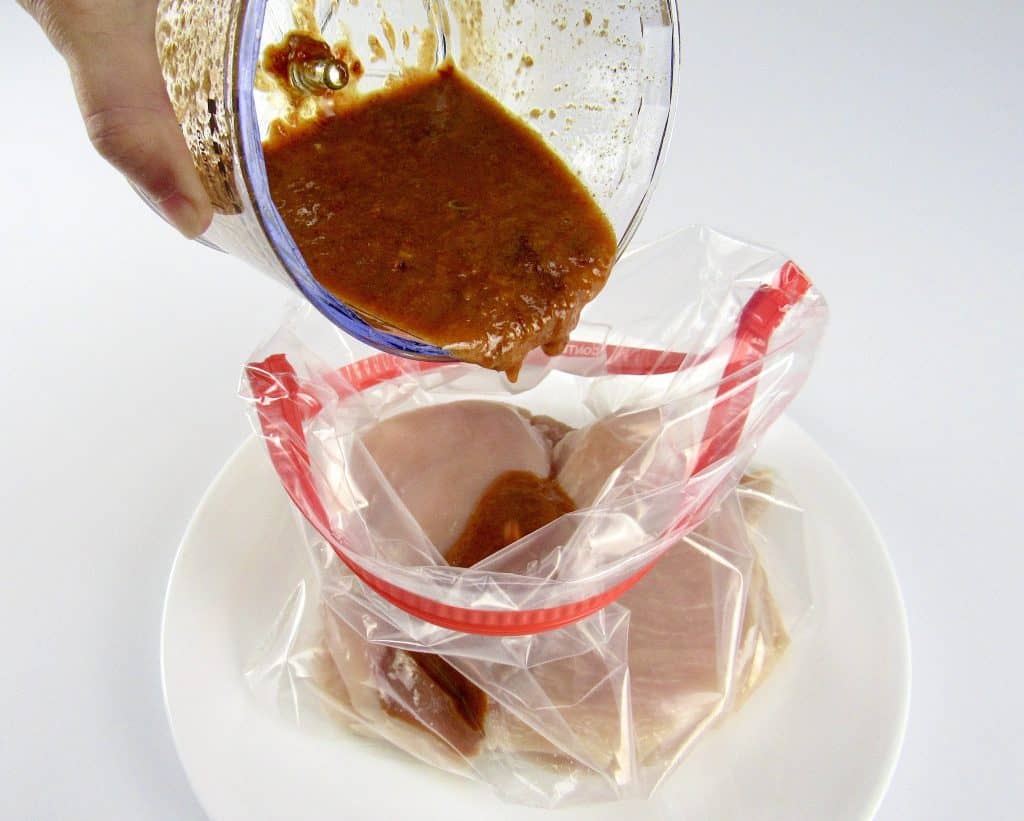 chicken in a food storage bag with marinade being poured over the top