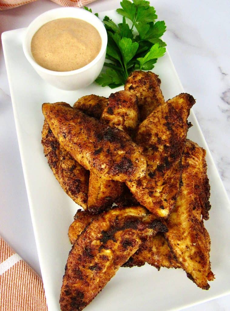 blackened chicken tenders on white plate with dipping sauce on side