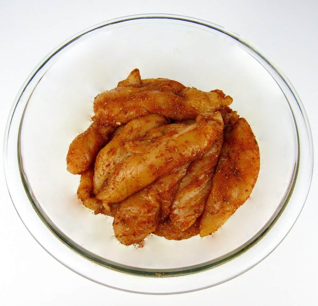 raw chicken tenders in glass bowl coated in blackened seasoning